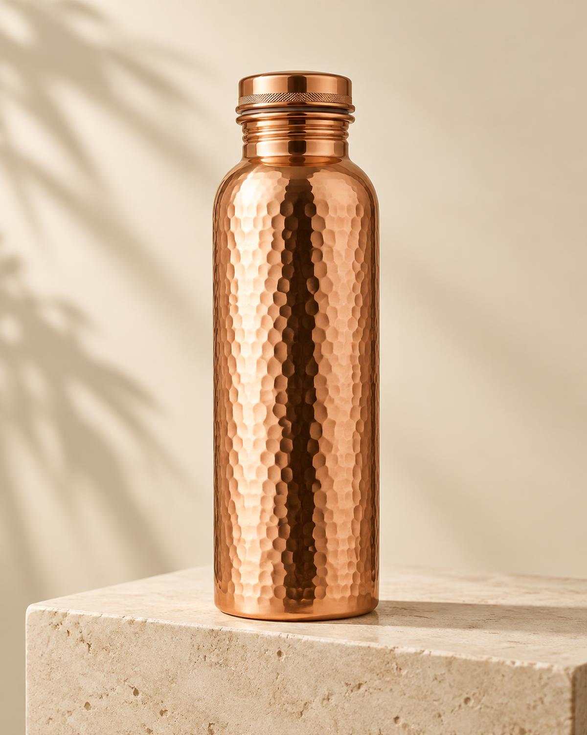 Hammered copper water bottle standing on an ivory stone plinth